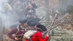 Revolutionary War Colonial soldiers take cover behind a low stone wall and fire their muskets